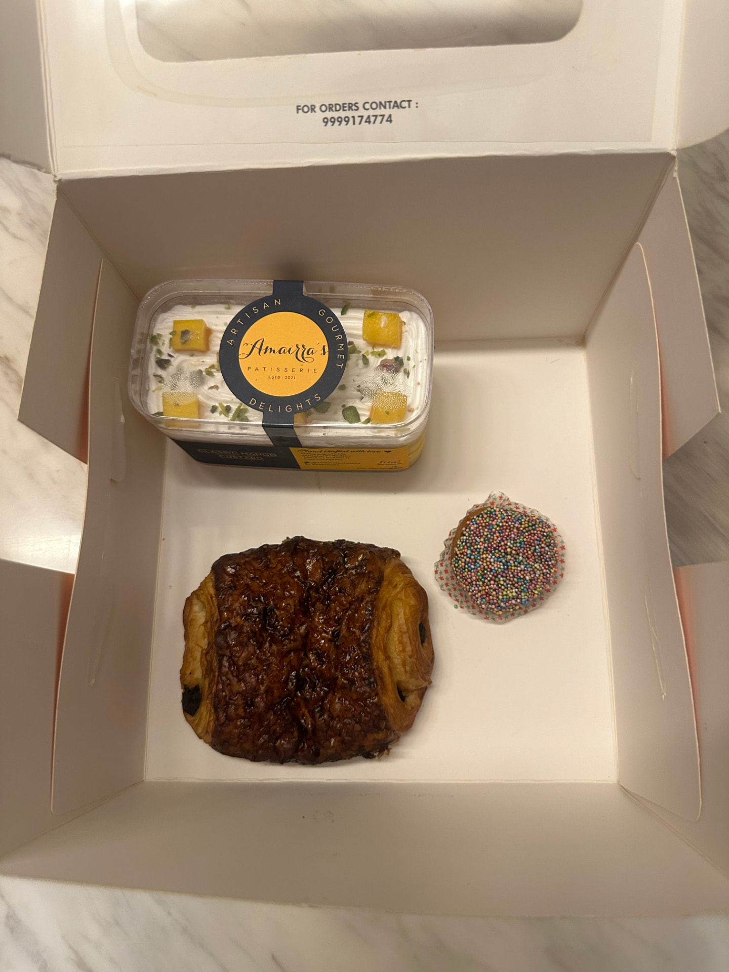 An Amairra's Patisserie mango custard tub with a pain au chocolat and sprinkle cookie